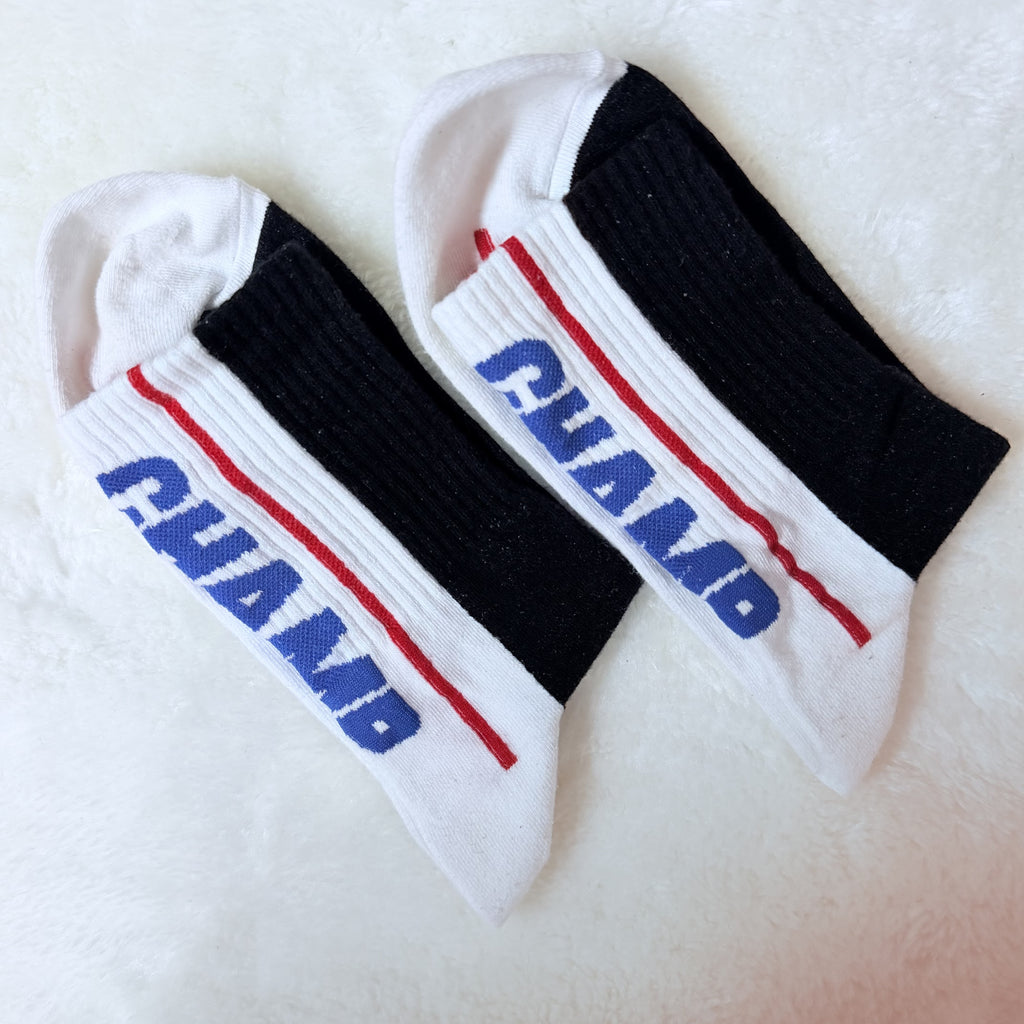 Athletic white and black crew socks featuring a bold vertical blue and red 'CHAMP' text design and sport stripes.