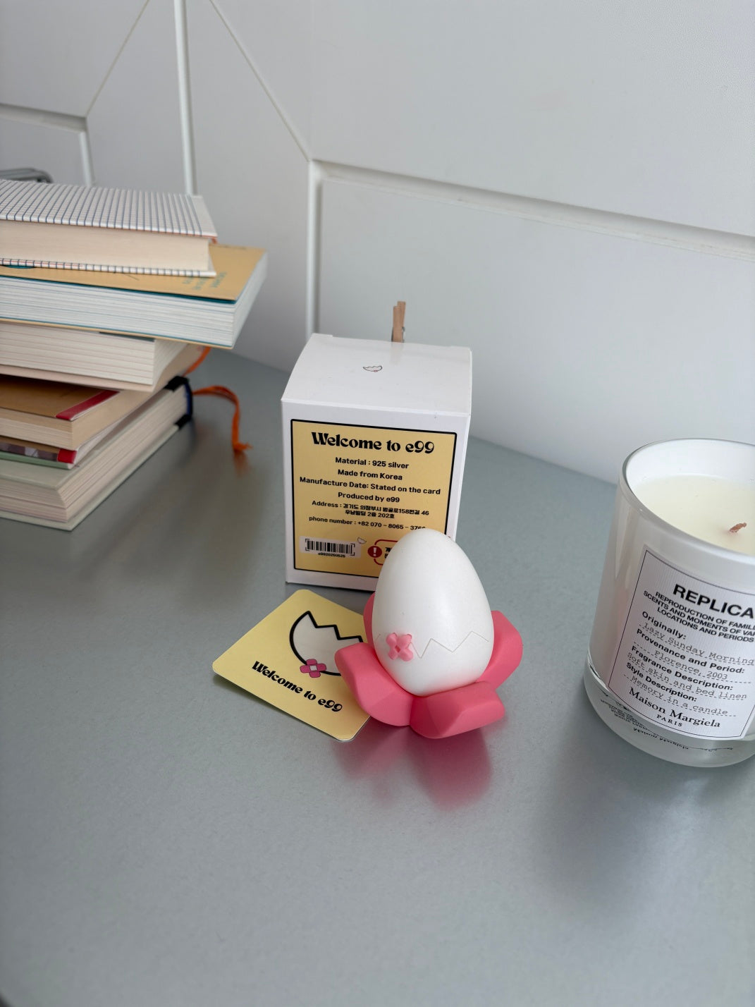 Small white egg case on a pink stand with a card and books in the background
