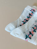 White sheer crew socks with mesh texture and a pink and green floral vine along the side, worn on feet.