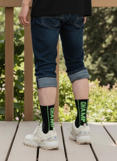 Person wearing blue jeans and white sneakers with green socks featuring the word 'Champ' on a wooden deck.