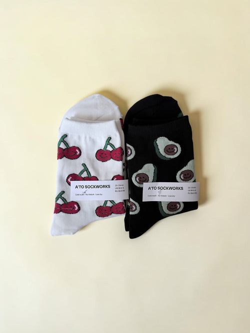 Two pairs of socks with cherry and avocado patterns on a beige background