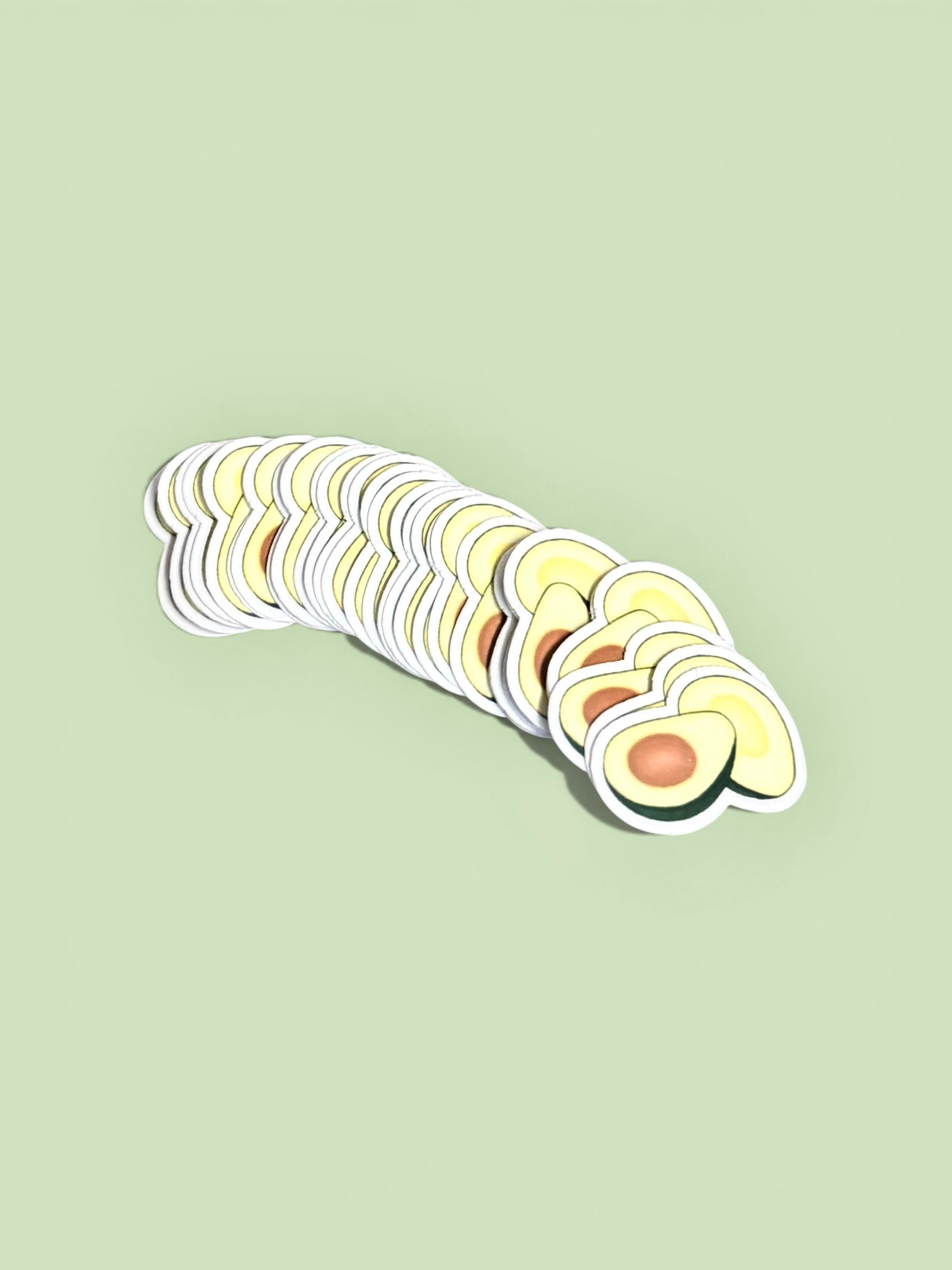A stack of cute avocado die-cut stickers displayed on a soft green background.